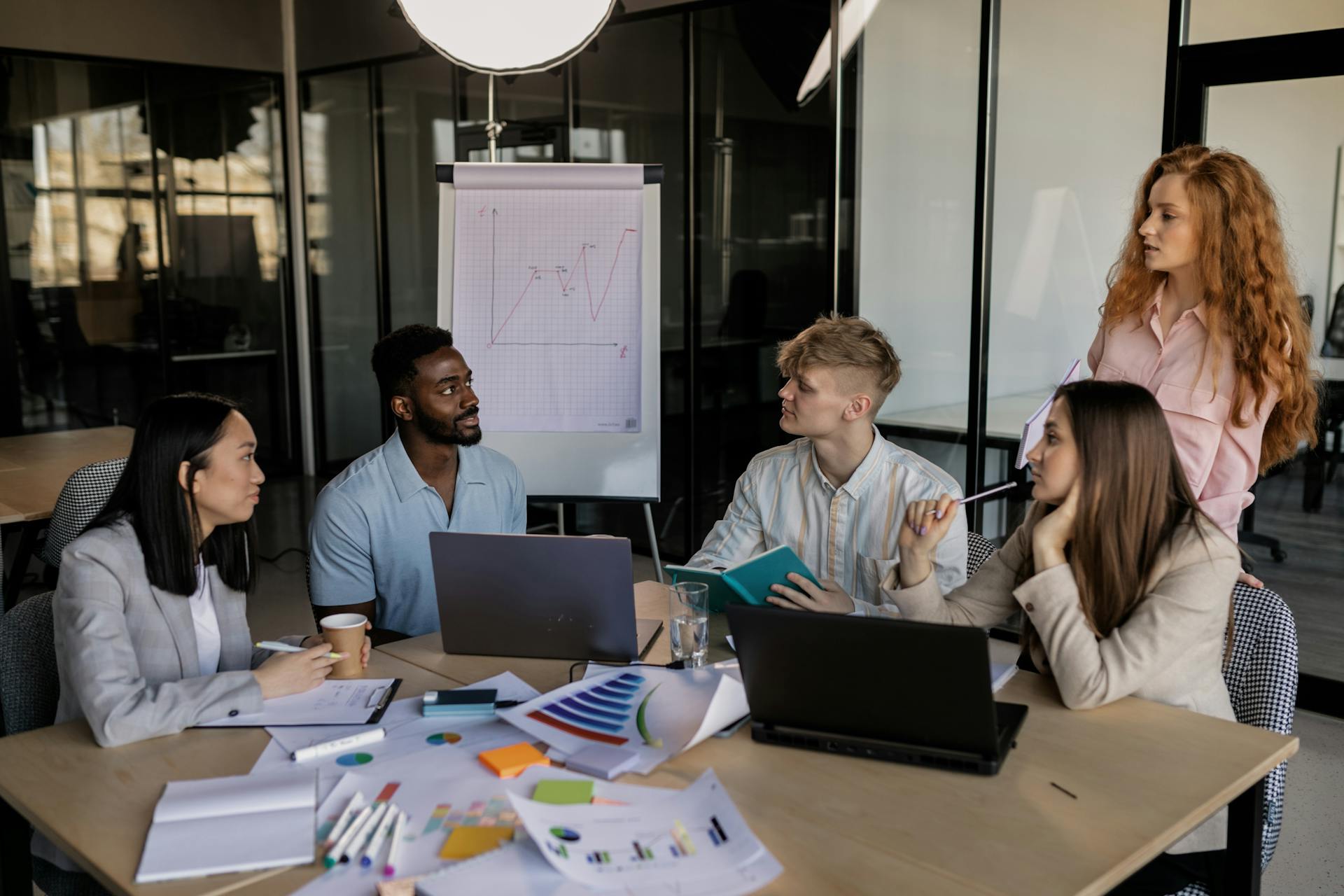 A team meeting around a table with laptops and color swatches in a glass-walled office.